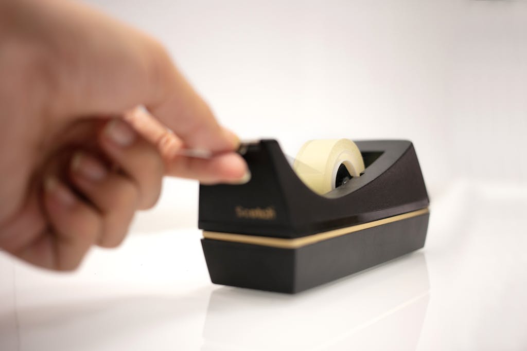 Serlig: A close-up of a hand using a tape dispenser on a clean white background.