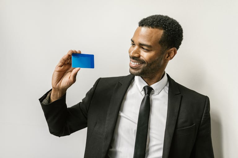 Magento Service Gonzay A confident man in a suit holds a credit card, smiling towards it.