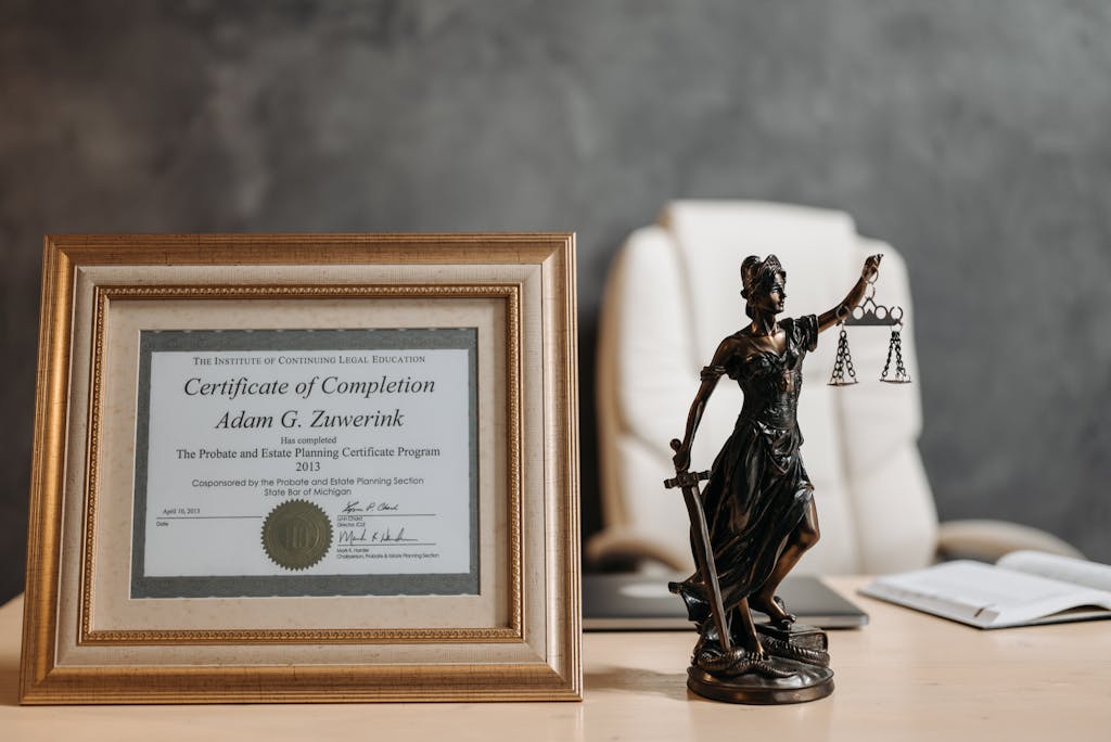 Bolly4u Me A framed legal certificate and Lady Justice figurine on a desk in a law office setting.