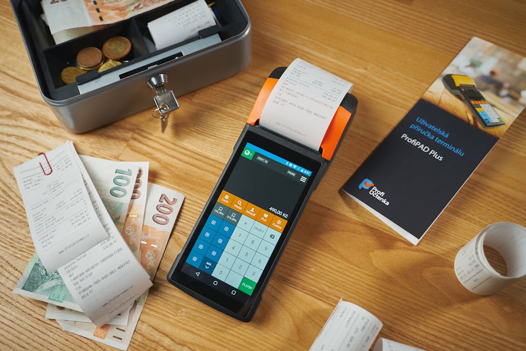 Simbramento A modern payment terminal with receipts, cash, and manual on a wooden table.