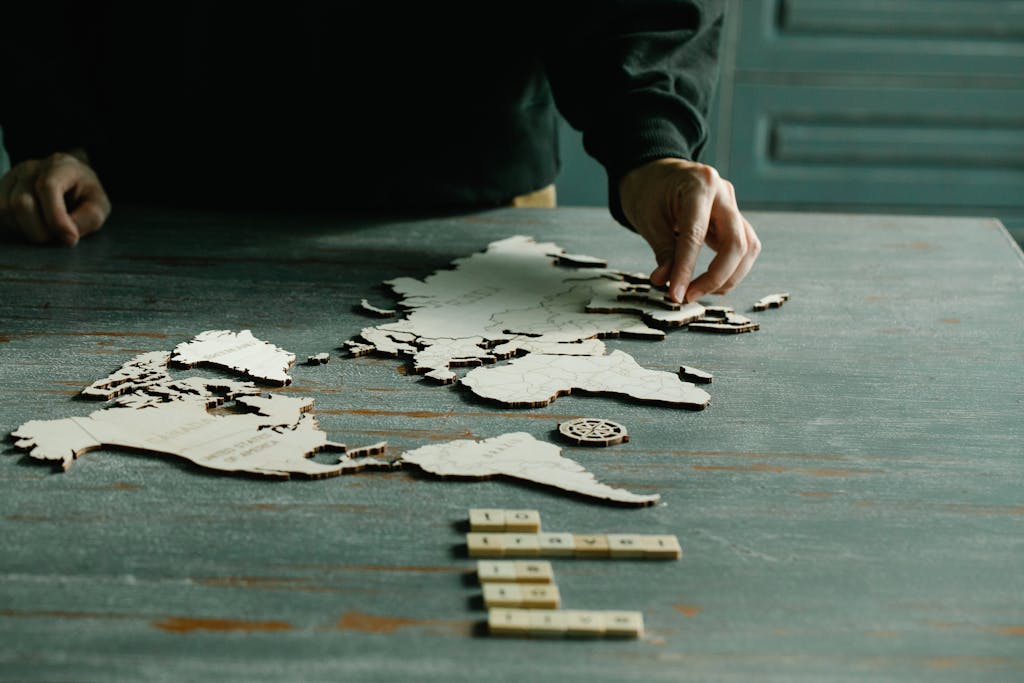 VirtusPlays A person arranging a wooden puzzle of a world map on a rustic wooden table.