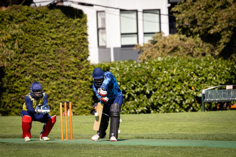 Wheon Cricket 07 Cricketer batting during an outdoor match with a wicketkeeper behind on a sunny day.