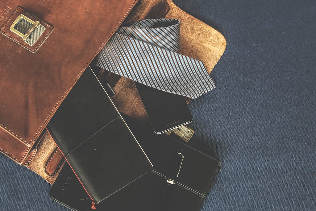 Blazertje Flat lay of men's leather bag with accessories like a tie, notebook, and phone. Ideal for business themes.