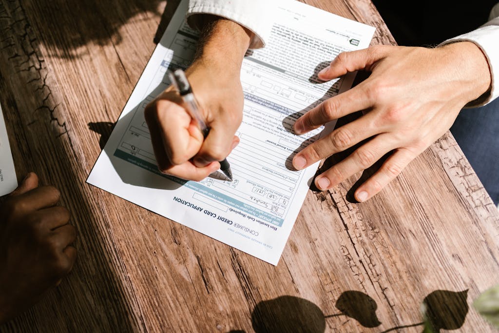 Simbramento Hands writing on a consumer loan credit application form on a wooden table.