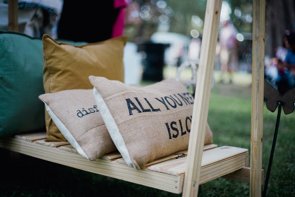 Akrylika Outdoor cushions display with 'All You Need Is Love' slogan on burlap texture.