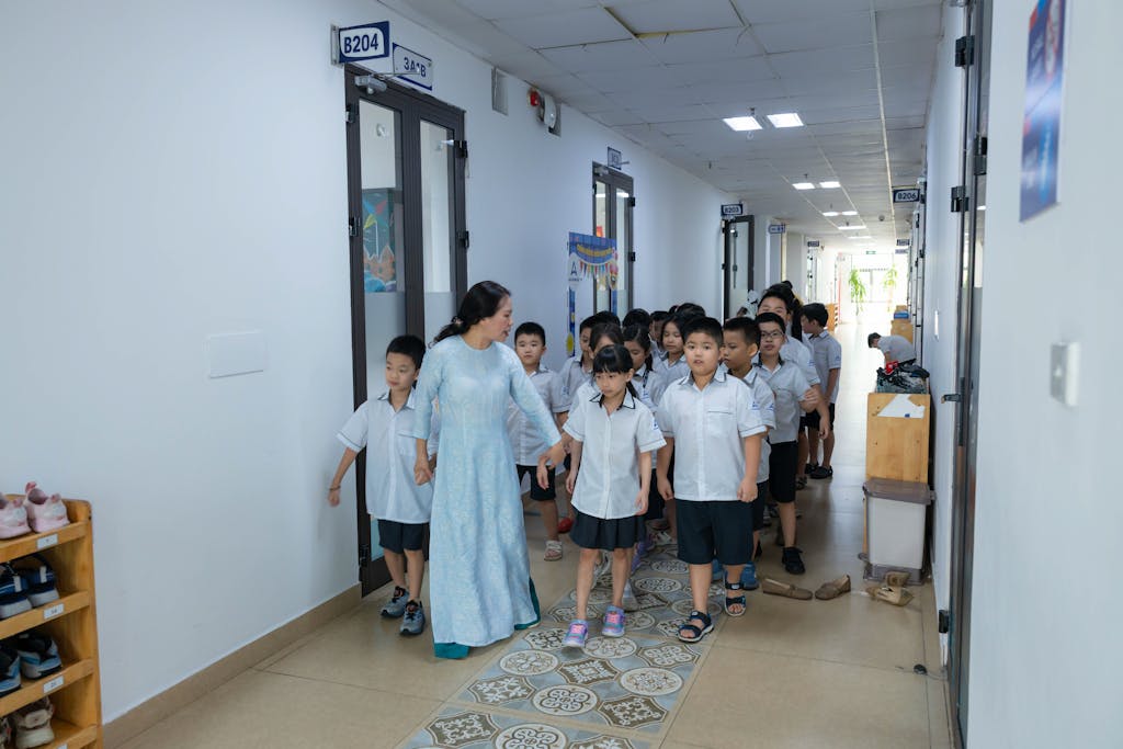 Dainikshiksha com bd Teacher guiding students in uniform through school corridor.
