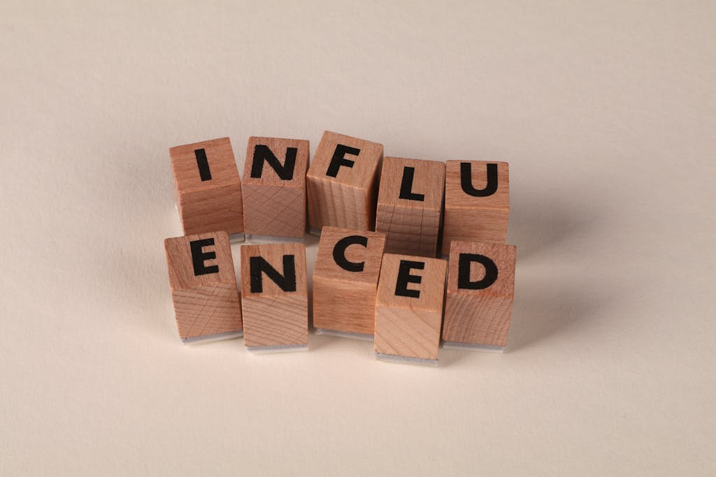 uyç Wooden letter blocks arranged to spell 'Influenced' on a neutral beige surface.