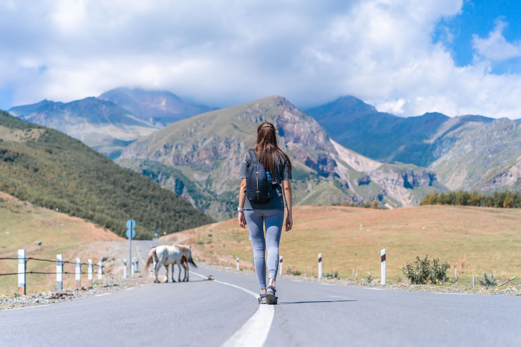Together Toward Together TowardBack view of woman with backpack walking on road in Stepantsminda, Georgia's stunning mountains.